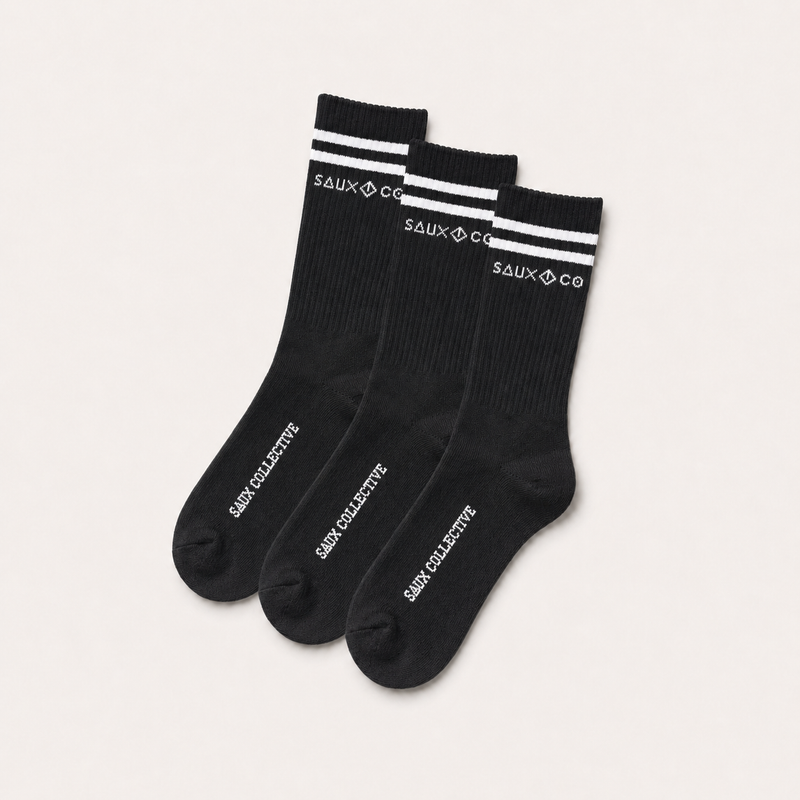 Three black crew socks with white stripes and white branding text on the cuffs and soles, arranged in a fan shape on a light beige background.